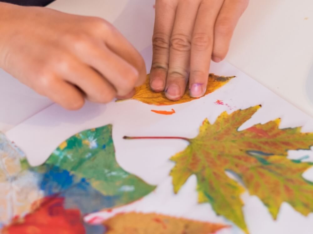 Hands of a child creating art with leaves and paint